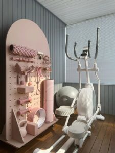 Home gym with white treadmill and pink wall organiser for equipment.
